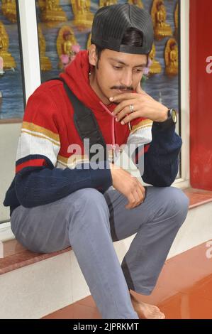 Un jeune homme portant une casquette en arrière en regardant vers le bas tout en étant assis sur les escaliers Banque D'Images