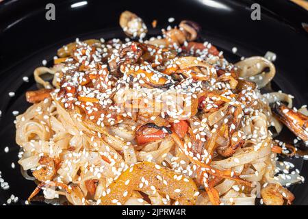 Nouilles Udon à la viande, aux champignons et aux légumes. Parsemé de graines de sésame. Cuisine asiatique, rôti sur fond noir, espace copie Banque D'Images