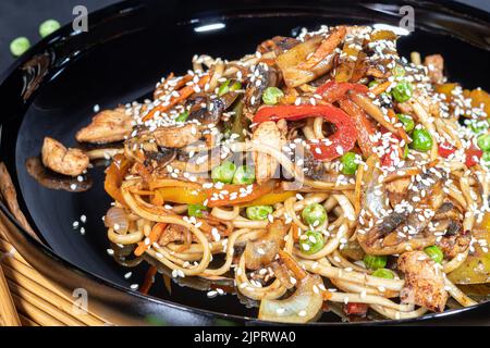 Nouilles Udon à la viande, aux champignons et aux légumes. Parsemé de graines de sésame. Cuisine asiatique, rôti sur fond noir, espace copie Banque D'Images