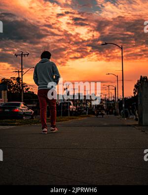 Photo verticale d'une personne marchant près de la plage d'Alki sous un ciel de coucher de soleil orange vif Banque D'Images