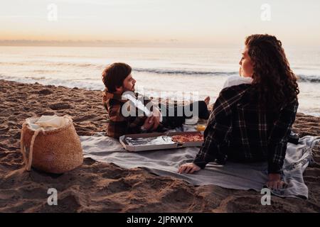 Jeune couple pique-nique sur la plage à l'aube, femme et homme se rencontrent au lever du soleil ensemble sur la mer Banque D'Images