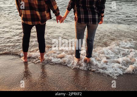 Couple méconnaissable se rencontrant au lever du soleil sur la mer, homme et femme tenant par les mains debout dans l'eau Banque D'Images