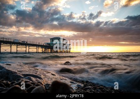 Août 2022, île de Wight, Royaume-Uni. Coucher de soleil à Totland Bay avec des vagues s'écrasant sur les rochers, et la jetée en arrière-plan avec un ciel magnifique. Banque D'Images