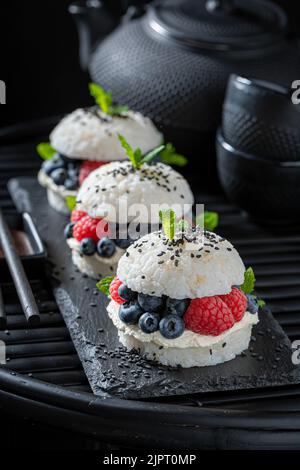 Délicieux hamburger à sushis frais avec framboises et bleuets sur une assiette foncée. Dessert japonais à base de fruits et de riz. Banque D'Images