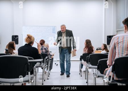 Au cours d'un test de physique à l'université, un professeur en veste fait le tour du public et communique avec les étudiants qui écrivent et répondent aux questions. Banque D'Images