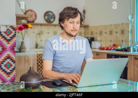Diffuseur d'huile essentiel sur la table en cours de cuisson pendant que l'homme utilise un ordinateur portable Banque D'Images