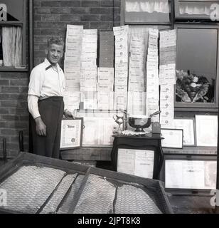 1955, historique, gagnant du prix du jardinage, en dehors de sa maison d'entreprise, un gentleman montrant le grand nombre de certificats primés qu'il a gagné pour le jardinage prouesse, Angleterre, Royaume-Uni. La plupart d'entre eux ont reçu le premier prix des spectacles de légumes, fruits et fleurs de la Corporation of Stockport. Banque D'Images