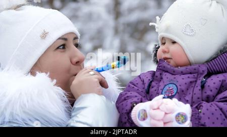 Dans le fond de la forêt d'hiver, une jeune femme, maman tient ses mains et s'amuse d'une fille d'un an. Elles sont vêtues de chapeaux drôles de bumbon. Photo de haute qualité Banque D'Images