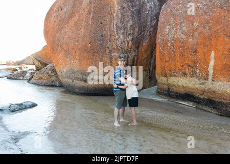 Un père et un fils portant des lunettes de soleil et un chapeau à côté de rochers sur la plage de Squeaky dans le promontoire de Wilson, dans le sud du Gippsland, en Australie Banque D'Images