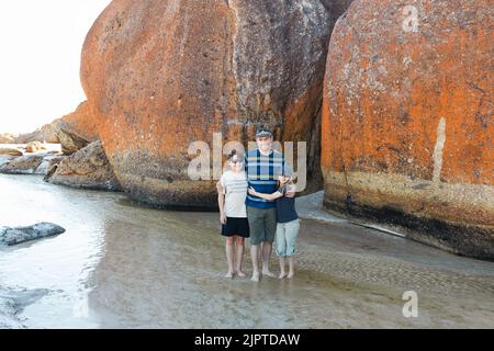 Un père, une fille et un fils portant des lunettes de soleil et un chapeau à côté de rochers sur la plage de Squeaky dans le promontoire de Wilson, dans le sud du Gippsland, en Australie Banque D'Images