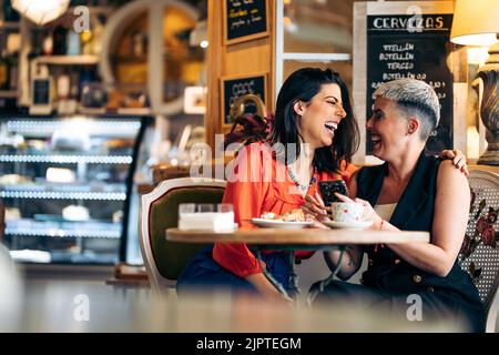 Deux amies adultes rient tout en regardant le mobile et en buvant du café Banque D'Images