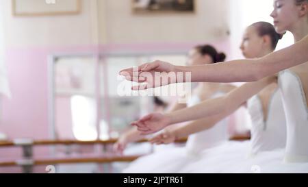 Dans la salle de ballet, les jeunes ballerines effectuent des allonge, en déplaçant les mains élégamment vers le haut et vers le bas, en gros plan. Photo de haute qualité Banque D'Images