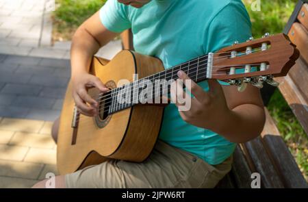 Le jeune homme joue les mains et sur une guitare acoustique classique en bois dans la rue. Gros plan sur la mise au point d'un adolescent jouant à la main des cordes d'un Banque D'Images