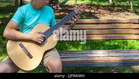 Le jeune homme joue les mains et sur une guitare acoustique classique en bois dans la rue. Gros plan sur la mise au point d'un adolescent jouant à la main des cordes d'un Banque D'Images