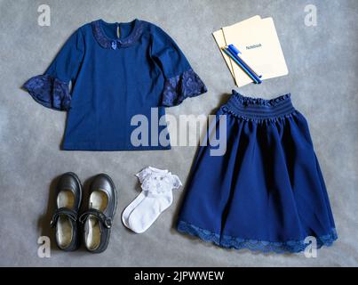 Uniforme scolaire pour petite fille sur fond gris, plat. Vue de dessus des vêtements pour étudiants, ensemble avec chaussures, jupe, chemise et carnets. Concept de premier Banque D'Images