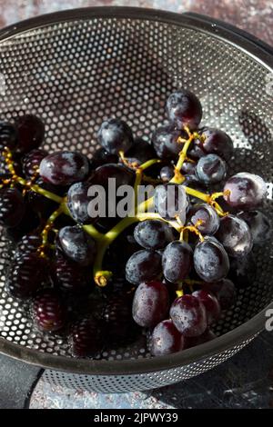 Bouquet de raisins noirs dans une passoire en métal. Sur un arrière-plan grunge Banque D'Images