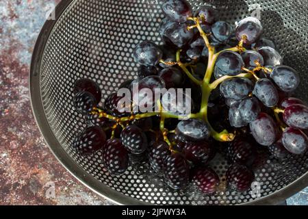 Bouquet de raisins noirs dans une passoire en métal. Sur un arrière-plan grunge Banque D'Images