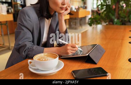 Jeune femme d'affaires utilisant une tablette numérique travaillant assis dans un café. Banque D'Images