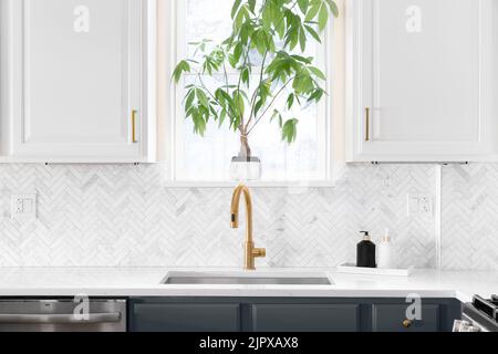 Détail lavabo dans une cuisine de luxe avec carreaux de dosseret à chevrons. Comptoir en marbre blanc et robinet en or. Banque D'Images