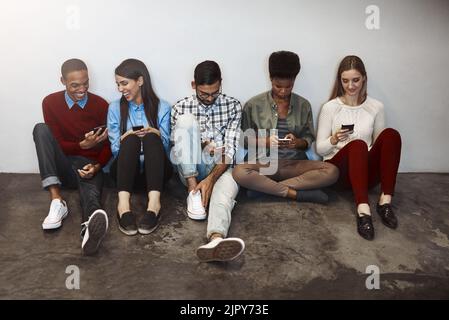 La vie sur le campus est une vie connectée. Groupe d'étudiants universitaires utilisant leur téléphone cellulaire sur le campus. Banque D'Images