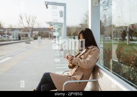 femme assise sur une gare regardant sa montre de poignet Banque D'Images