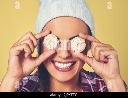 Ne soyez pas des bonbons pour les yeux, soyez de la nourriture pour l'âme. Une jeune femme couvrant ses yeux avec des biscuits sur un fond coloré. Banque D'Images