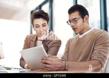 L'innovation s'épanouit lorsqu'ils se rassemblent : deux hommes d'affaires travaillent ensemble sur une tablette numérique dans un bureau. Banque D'Images