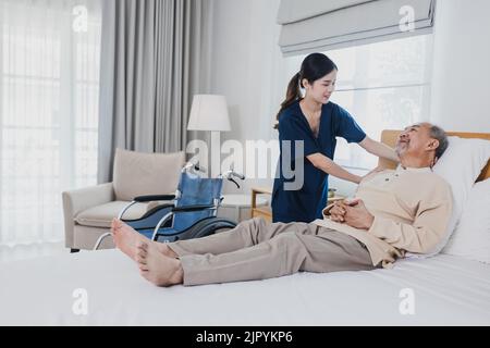 Un homme asiatique âgé allongé sur un lit reçoit une aide médicale pour des blessures par une infirmière asiatique, médecin femme aidant Banque D'Images