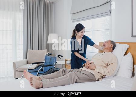 Un homme asiatique âgé allongé sur un lit reçoit une aide médicale pour des blessures par une infirmière asiatique, médecin femme aidant Banque D'Images