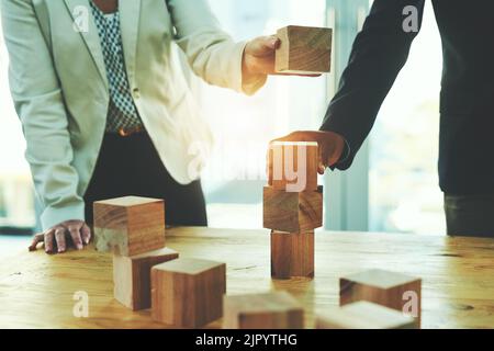 Le succès repose sur une base solide et stable. Deux hommes d'affaires méconnus empilent des blocs de bois ensemble dans un bureau. Banque D'Images