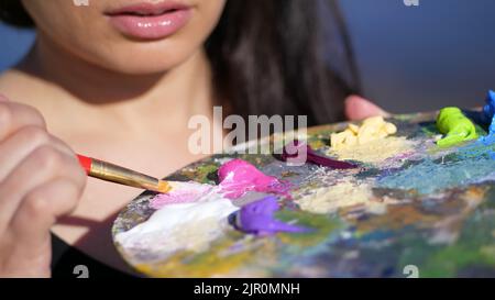 été, plein air, gros plan d'une palette avec des peintures, la femme artiste mélange des peintures avec un pinceau sur la palette. Photo de haute qualité Banque D'Images