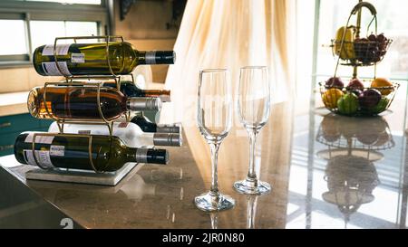 Un gros plan de bouteilles de vin avec des verres vides et un panier de fruits sur un comptoir Banque D'Images