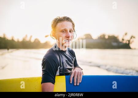 Portrait d'un jeune garçon avec des bretelles dentaires avec planche de surf va pour le surf.Il sourit et marche dans l'eau.Bonne enfance et vacances actives Banque D'Images