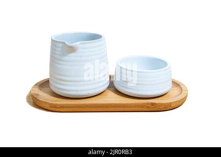 Un ensemble de mug en céramique et un pichet de thé, en argile blanche, sur une assiette en bois sur fond blanc. Banque D'Images