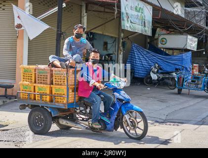 Employés sur un marché des fruits et légumes en Thaïlande, transportant des boîtes de fruits sur une moto. Banque D'Images