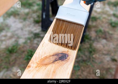 La femme imprègne des poutres de pin en bois rabotées avec des dimensions de 100x100mm avec une imprégnation incolore. Banque D'Images
