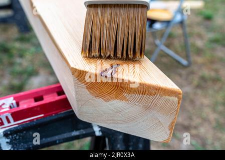 La femme imprègne des poutres de pin en bois rabotées avec des dimensions de 100x100mm avec une imprégnation incolore. Banque D'Images