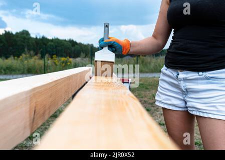 La femme imprègne des poutres de pin en bois rabotées avec des dimensions de 100x100mm avec une imprégnation incolore. Banque D'Images