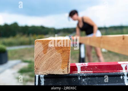 La femme imprègne des poutres de pin en bois rabotées avec des dimensions de 100x100mm avec une imprégnation incolore. Banque D'Images