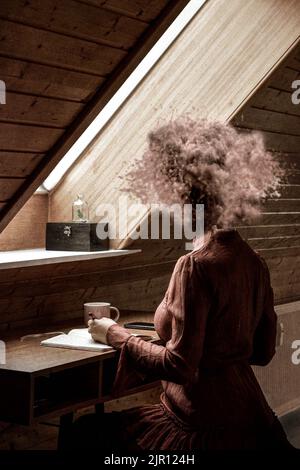 imagerie conceptuelle. Femme assise à côté d'une fenêtre écrivant et sans tête. La tête explose en raison de la contrainte. La femme a insisté pour essayer de se calmer Banque D'Images