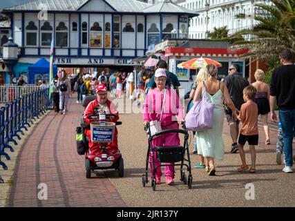 Un couple handicapé utilise un scooter de mobilité et un roller sur la promenade à côté de Eastbourne Pier, East Sussex, Royaume-Uni. Banque D'Images