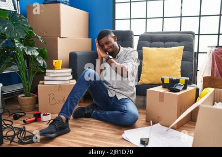 Homme afro-américain assis sur le sol dans une nouvelle maison dormant fatigué rêvant et posant avec les mains ensemble tout en souriant avec les yeux fermés. Banque D'Images