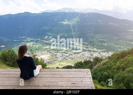 Vue de dessus du village de Mestia depuis le point d'observation Croix dans la région du Haut-Svaneti, Géorgie. Jeune femme méconnaissable assise et regardant Mestia d'en haut Banque D'Images