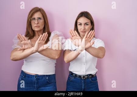 Mère hispanique et fille portant un t-shirt blanc décontracté sur fond rose rejet expression croisant les bras et les paumes faisant signe négatif, en colère Banque D'Images