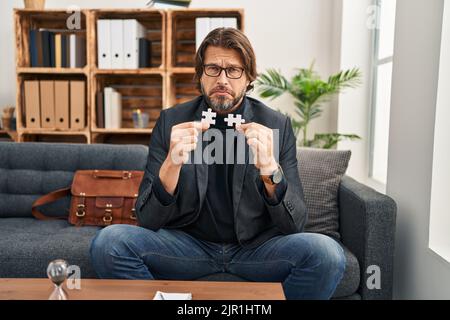 Beau homme d'âge moyen au bureau de consultation tenant des pièces de puzzle déprimé et s'inquiéter de la détresse, pleurant en colère et peur. Expression triste. Banque D'Images