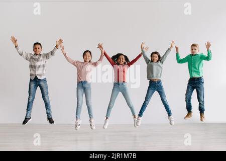 Groupe d'enfants joyeux et divers qui sautent les bras à l'intérieur Banque D'Images