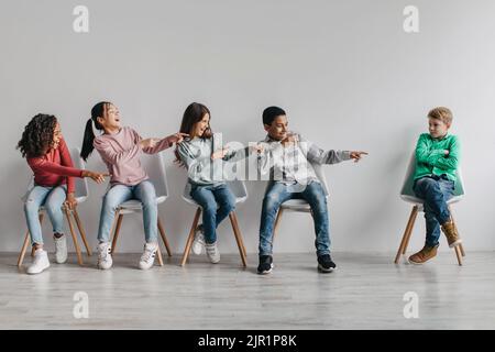 Divers camarades de classe enfants riant le doigt pointant vers un écolier victimisé en intérieur Banque D'Images