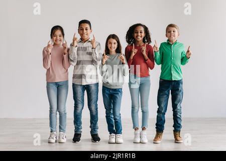 Joyeux et multiculturel enfants qui pointent les doigts vers le haut debout ensemble à l'intérieur Banque D'Images