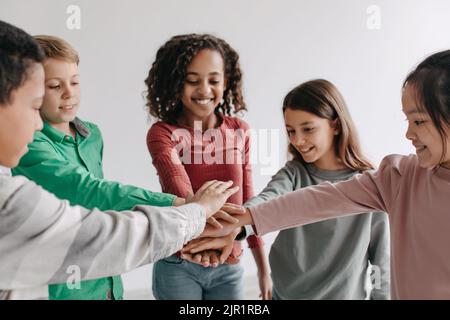 Joyeux préadolescents les enfants qui mettent les mains ensemble posent debout à l'intérieur Banque D'Images