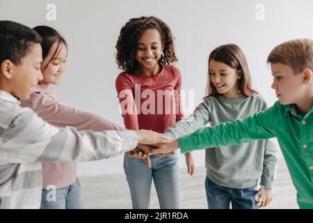 Joyeux enfants de la Préadolescence empiler les mains ensemble debout dans le cercle à l'intérieur Banque D'Images